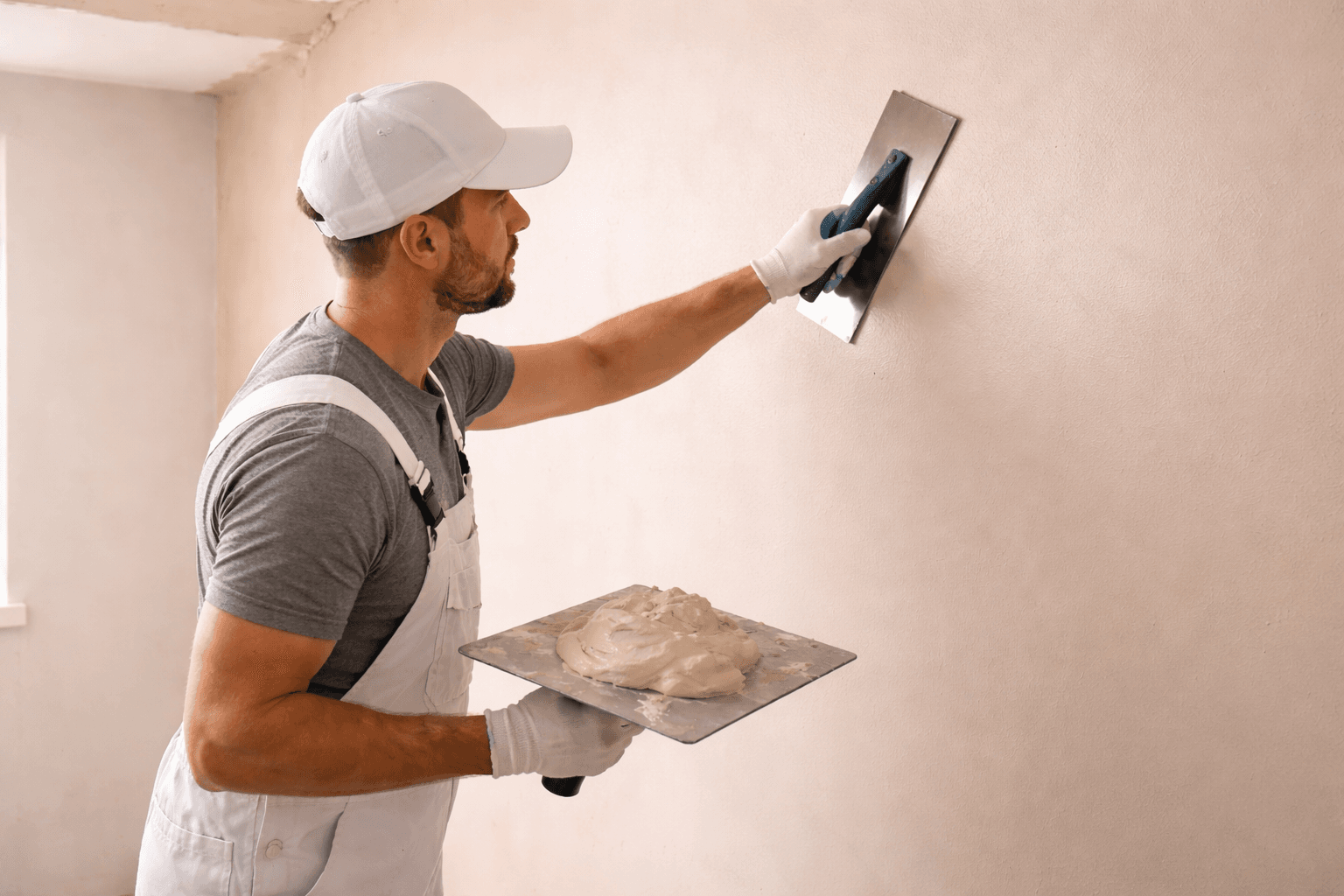 Professional plasterer smoothing an interior wall with trowel and hawk